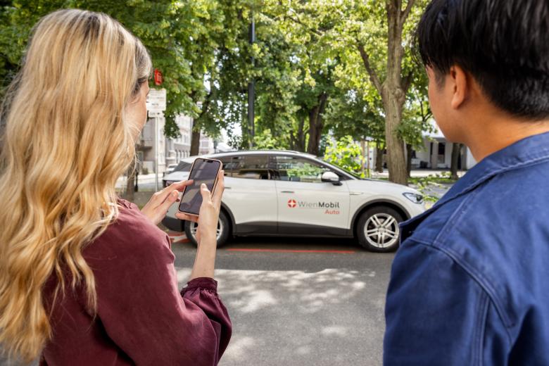 2 persons looking at a smartphone before the backdrop of a WienMobil car