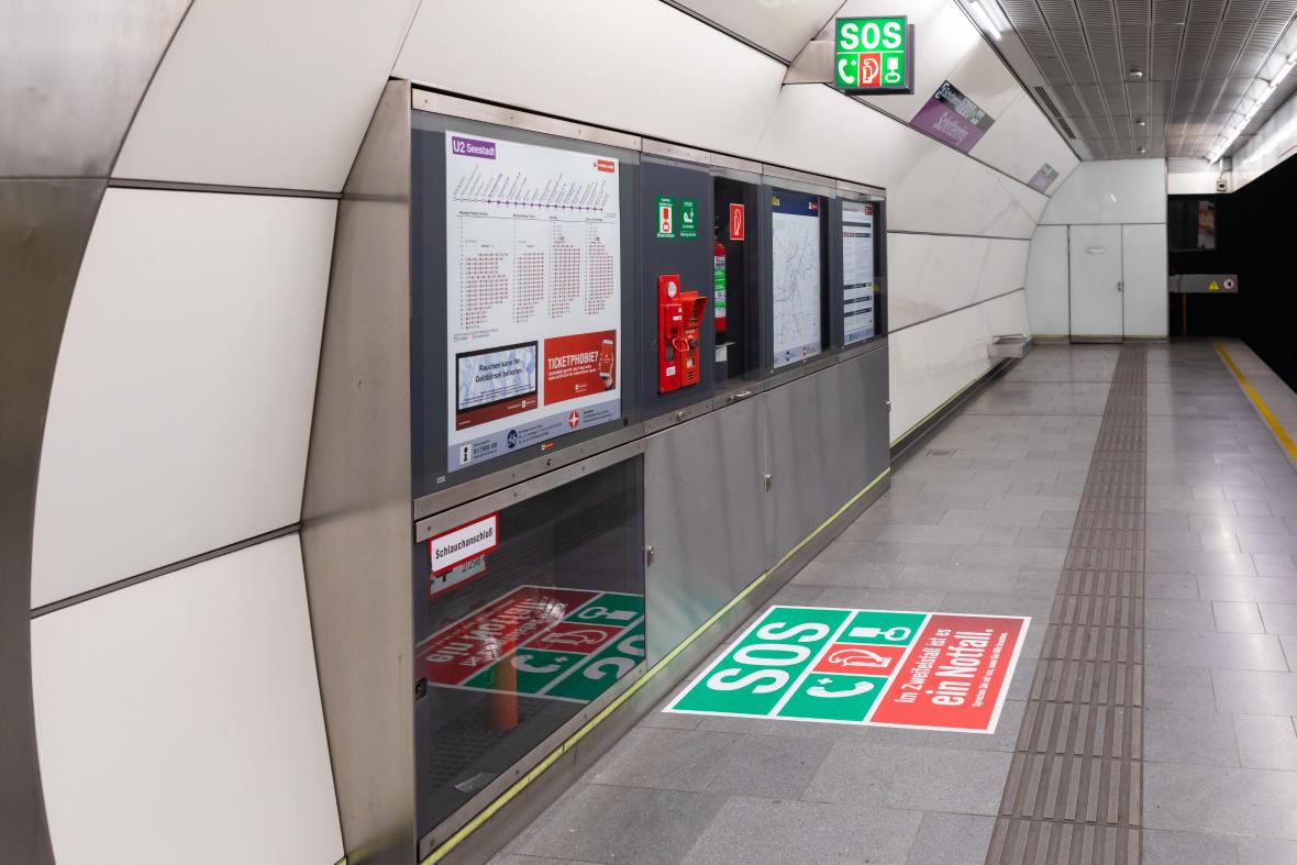 grüner SOS Würfel über dem Bahnsteig in der Ubahn Station und Aufkleber am Boden zeigen an wo die Sicherheitseinrichtungen sind