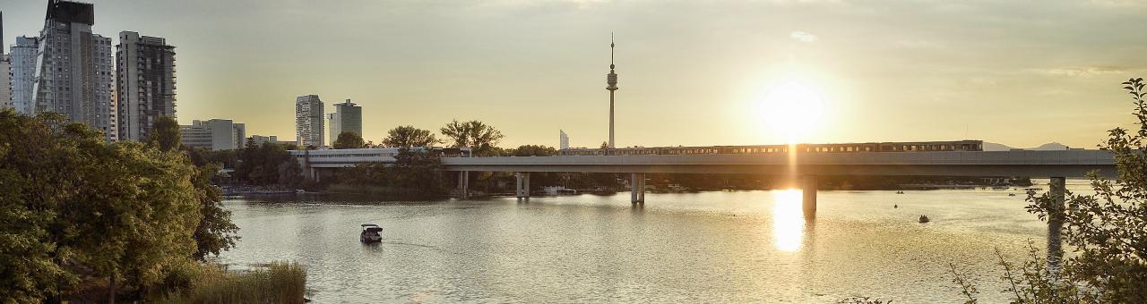 eine Ubahn fährt bei Sonnenuntergang über die Brücke über die Alte Donau
