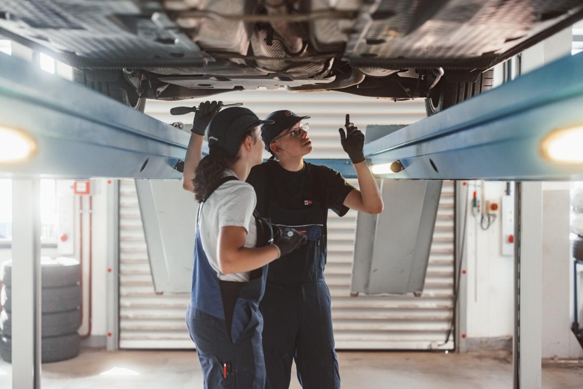 young woman and young man working on the underbody of a bus