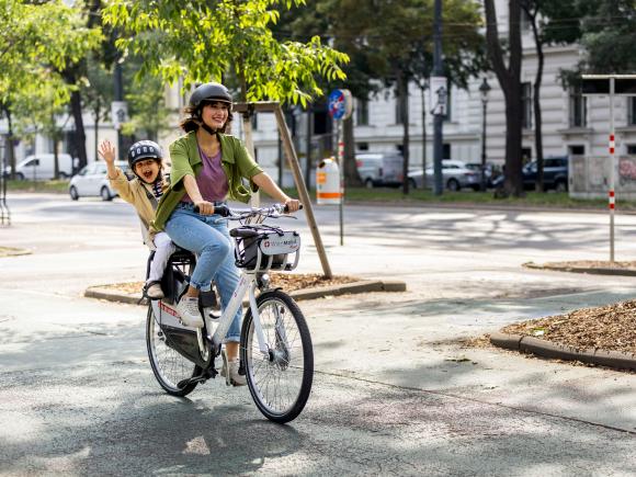 junge Frau und Kind im Kindersitz fahren mit WienMobil Rad durch die Stadt