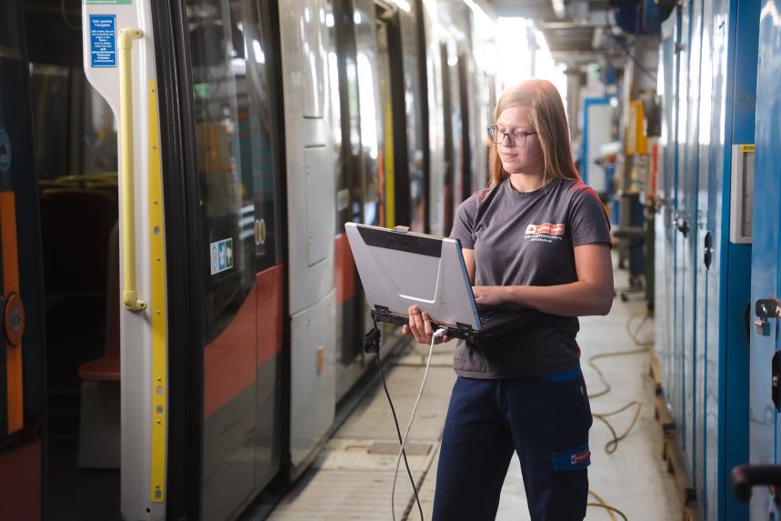 young woman in Wiener Linien work clothes holding a laptop computer and working on an ULF tramway