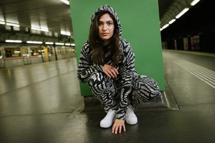 Junge Frau hockt mit schwarz-weißen Wiener-Linien-Jumpsuit in der U-Bahn-Station