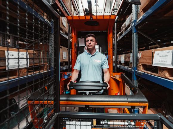a young man in a high-bay warehouse driving a forklift truck