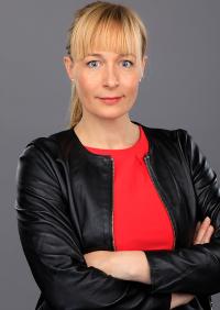 woman in a black jacket with blonde hair looks at the camera