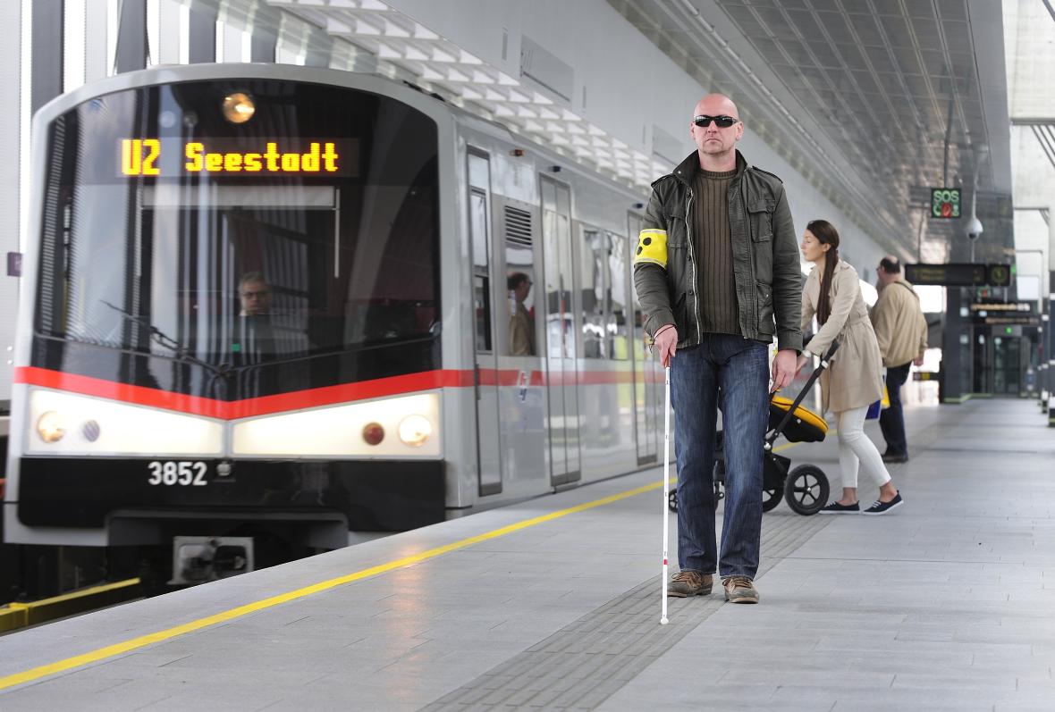 A man holding a cane for the blind is walking on a tram platform using the tactile orientation system